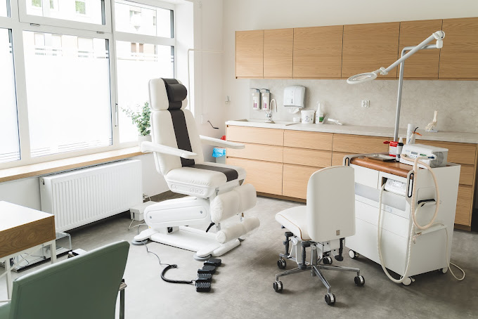 Gabinet zabiegowy PodoMed — fotel podologiczny przy dużym oknie, lampa z lupą i sprzęt zabiegowy